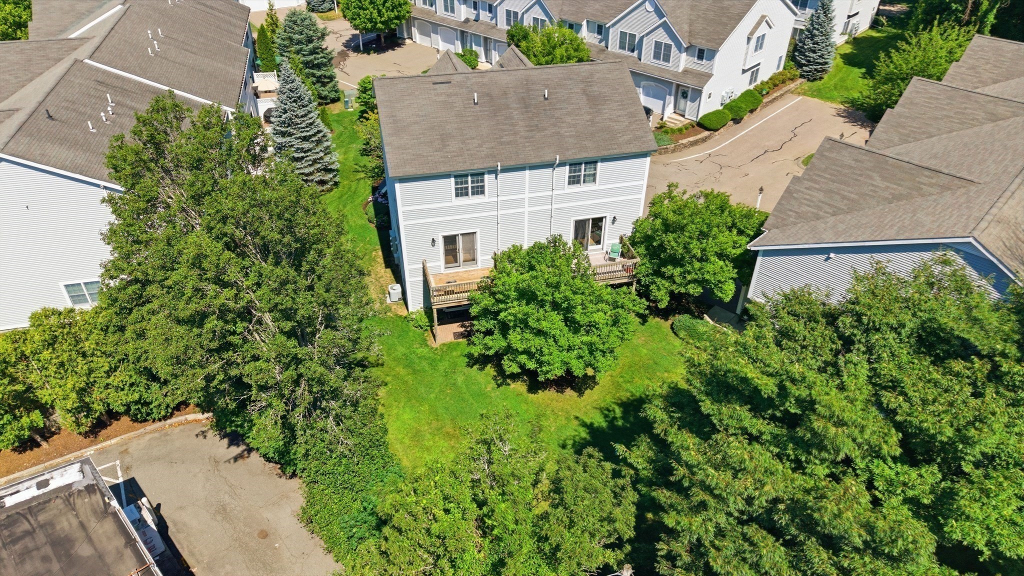 Aerial view of a white condominium building’s rear deck, lawn, and surrounding trees.