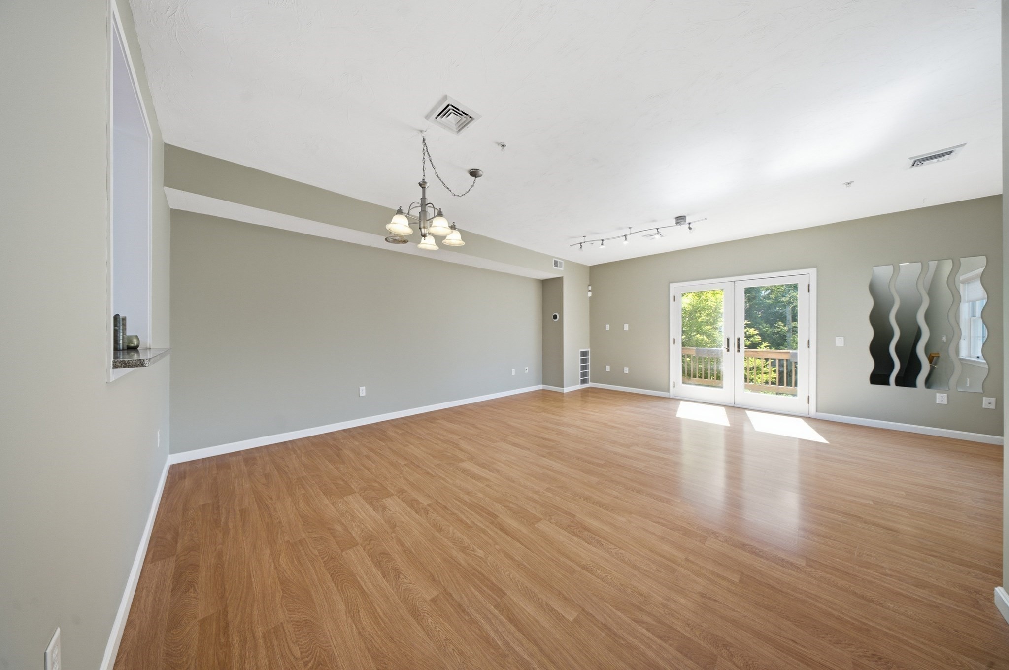 Empty living and dining area with wood-look floors, a chandelier, French doors, and wavy mirrors.