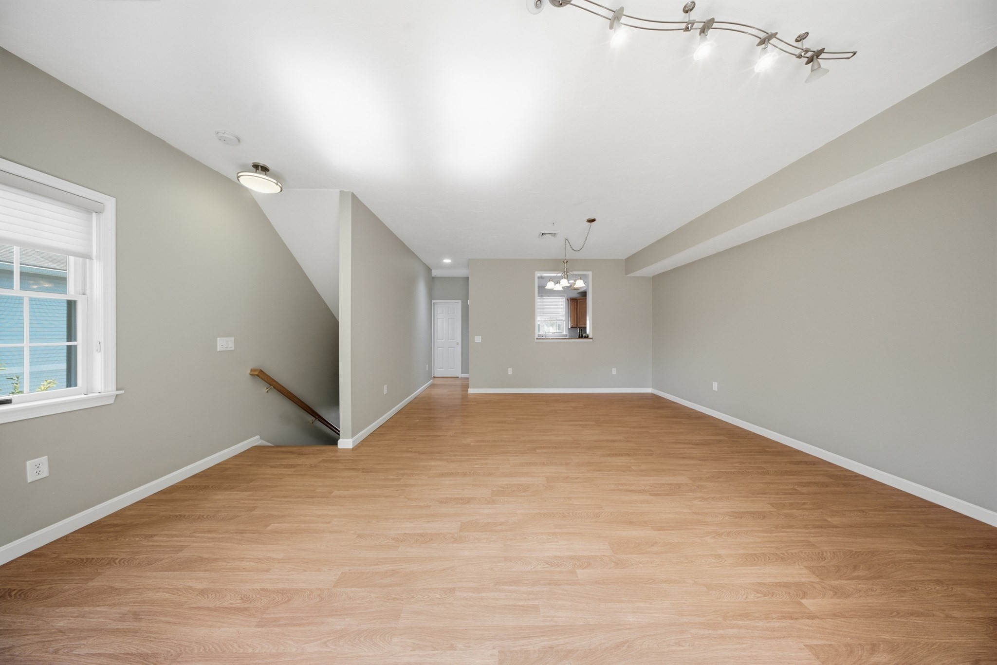 Vacant living and dining area with light wood floors, a window, and an open stairwell.