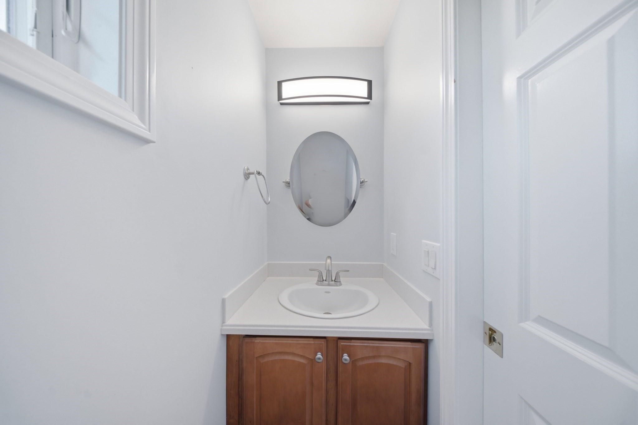 Bathroom vanity with an oval mirror, white countertop, and warm wood cabinets.