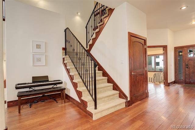 Foyer with a carpeted staircase, wrought-iron railings, hardwood floors, and a digital piano.