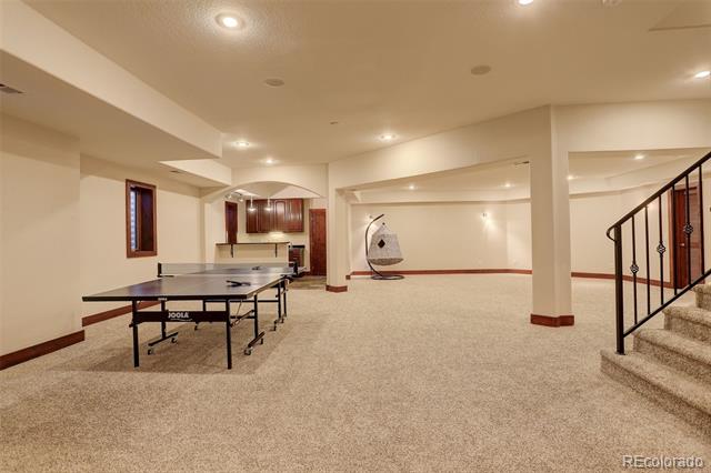 Finished basement recreation room with a ping-pong table, kitchenette, and carpeted staircase.