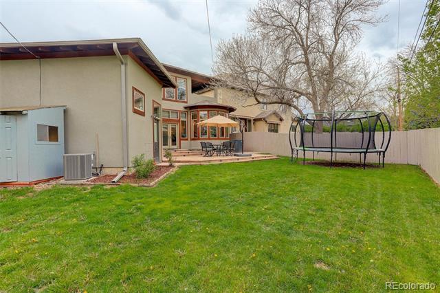 Backyard with a broad lawn, raised patio, outdoor dining set, and trampoline.