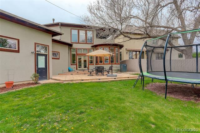 Home’s rear patio with outdoor dining set and umbrella, green lawn, and trampoline.