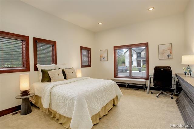 Bedroom with a white-covered bed, wood-trimmed windows, and a desk.