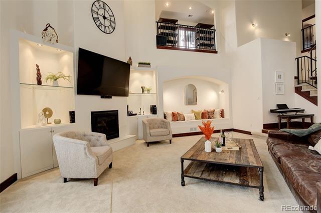Double-height living room with built-in shelves, fireplace, loft railing, and leather sectional.