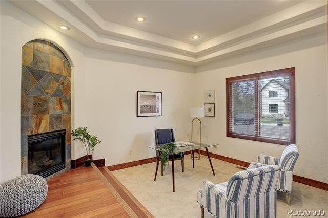 Sitting room with a tiled arched fireplace, glass-top table, and striped armchairs by a large window.