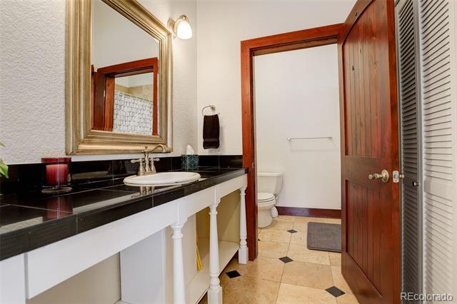 Bathroom with a black countertop vanity, framed mirror, and toilet beyond an open wooden door.