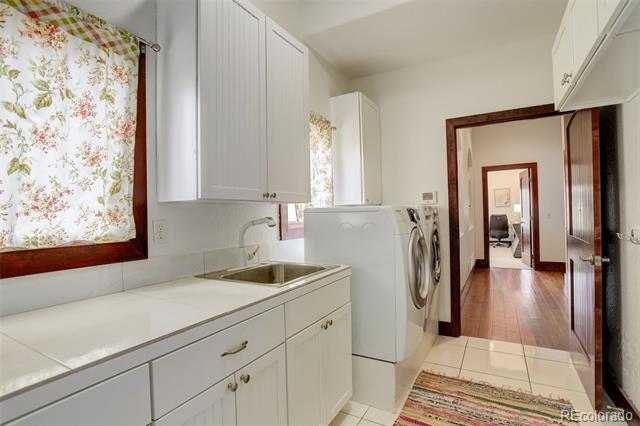 Laundry room with white cabinetry, utility sink, washer and dryer, and floral window shade.