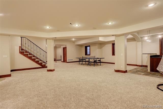 Finished basement recreation room with a carpeted floor, staircase, table, and kitchenette.