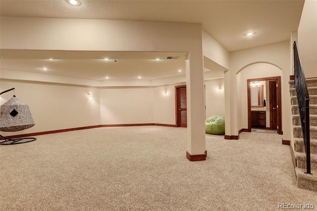 Finished basement recreation room with beige carpet, recessed lighting, a staircase, and a hanging chair.