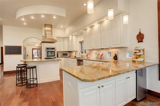 Bright kitchen with granite counters, white cabinetry, a large island, and hardwood floors.