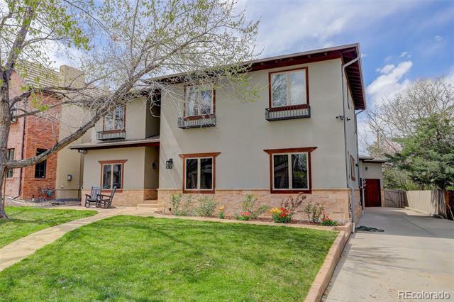 Two-story stucco home with a brick lower facade, front lawn, flower beds, and driveway.