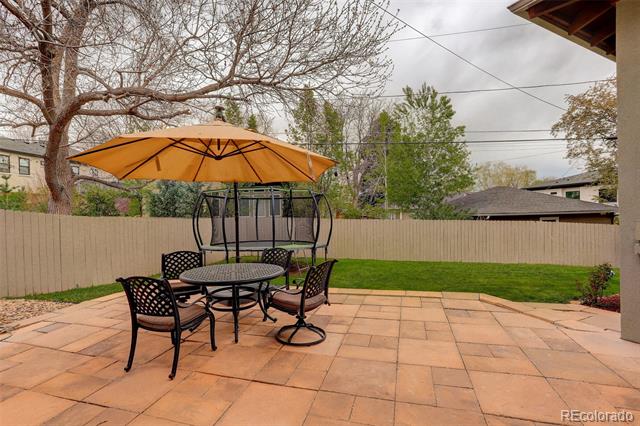 Backyard patio with tan pavers, an orange umbrella over a dining set, lawn, and privacy fence.