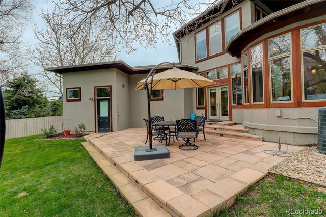 Rear patio with stone paving, table and chairs beneath an umbrella, beside a two-story home.