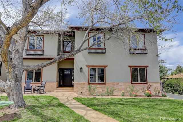 Two-story stucco house with stone lower facade, partly screened by a large tree.