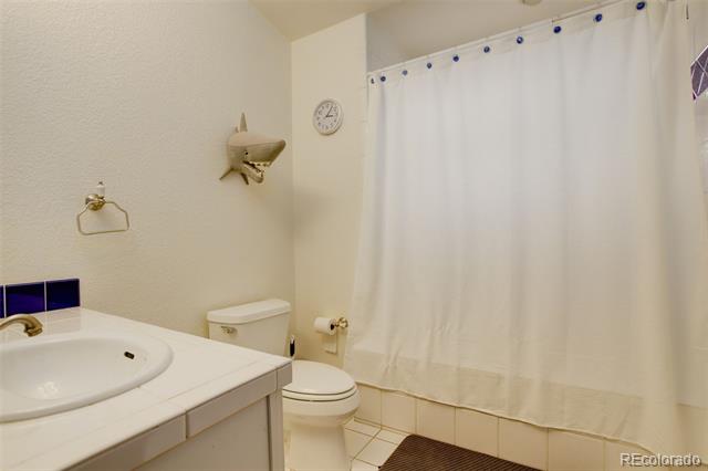 Bathroom with a white vanity, toilet, tiled floor, and full-length shower curtain.
