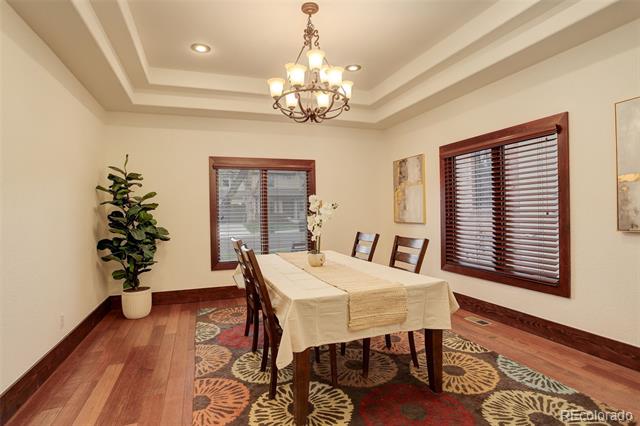 Dining room with a cream-covered table, chandelier, dark wood blinds, and patterned rug.