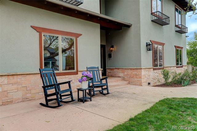Home entrance with stone facade, two rocking chairs, and a flower-topped table.