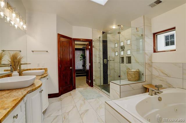 Bathroom with glass shower, soaking tub, and double vanity with stone countertops.