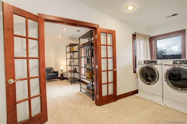 Laundry room with front-load washer and dryer beside open wood-and-glass French doors.