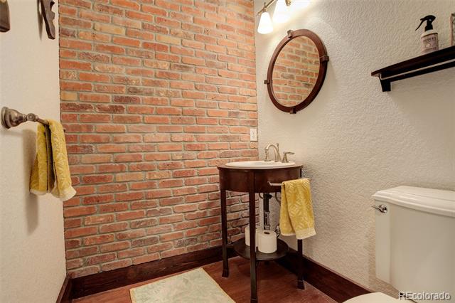 Bathroom with a red brick accent wall, dark wood vanity, round mirror, and yellow towels.