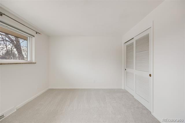 Empty carpeted room with a window overlooking bare trees and white louvered closet doors.