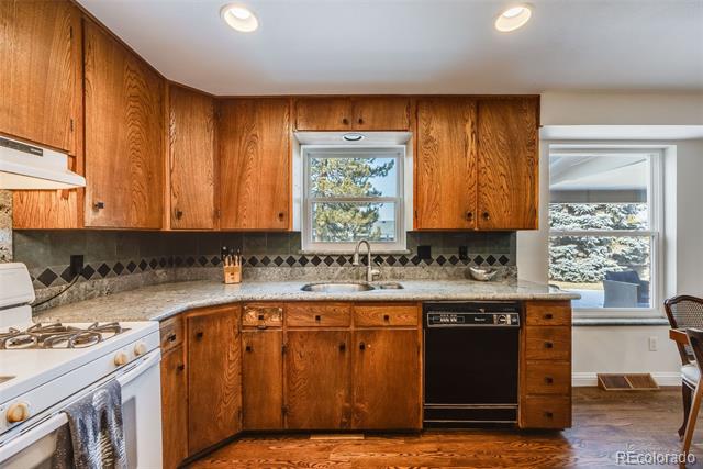 Kitchen with warm wood cabinets, granite counters, a black dishwasher, and windows overlooking trees.