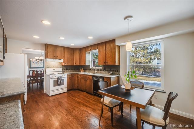 Kitchen with warm wood cabinets, hardwood floors, white appliances, and a dining table by a large window.