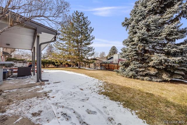 Snow-dusted backyard with a covered patio, outdoor seating, and mature evergreen trees.