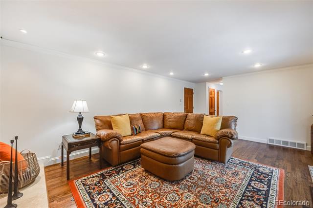 Living room with a brown leather sectional, ottoman, and colorful patterned rug.