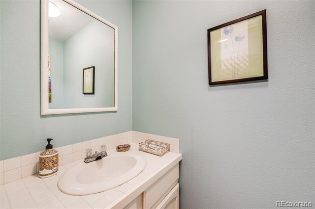 Bathroom vanity with tiled countertop, oval sink, large mirror, and framed floral artwork.
