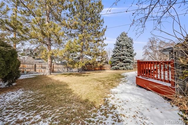 Snow-dusted backyard with mature trees, a wooden fence, and a red-railed deck.