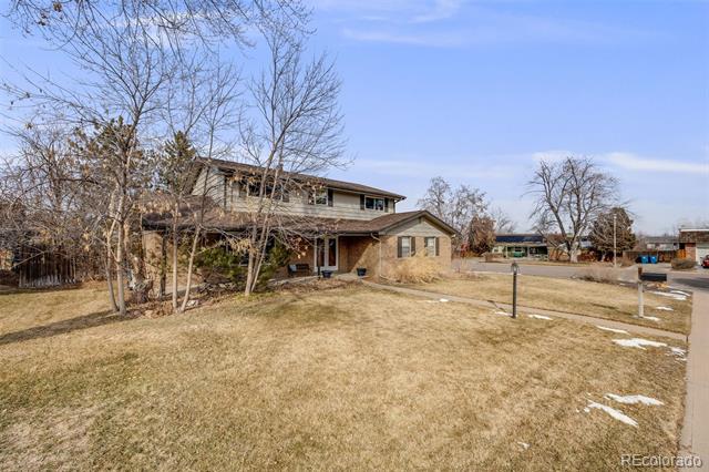 Two-story brick-and-siding home behind a wide dormant lawn, with leafless trees and patchy snow.