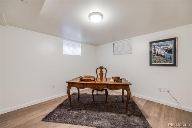 Furnished room with an ornate wooden table on a dark rug beneath two high windows.