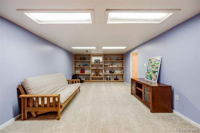 Basement living area with built-in shelves, a wooden-frame sofa, and colorful artwork by the media cabinet.