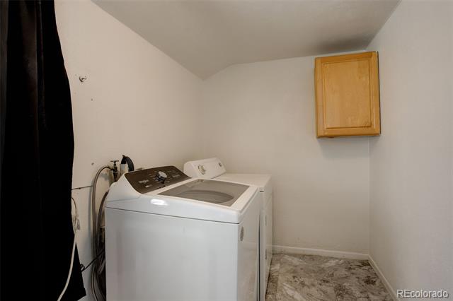 Laundry room with a white top-load washer, wooden wall cabinet, and stone-pattern tile floor.