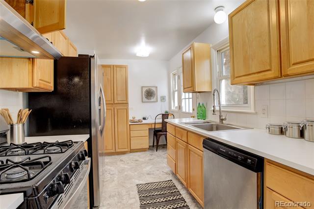Galley kitchen with honey-colored cabinets, black appliances, white countertops, and a stainless-steel dishwasher.