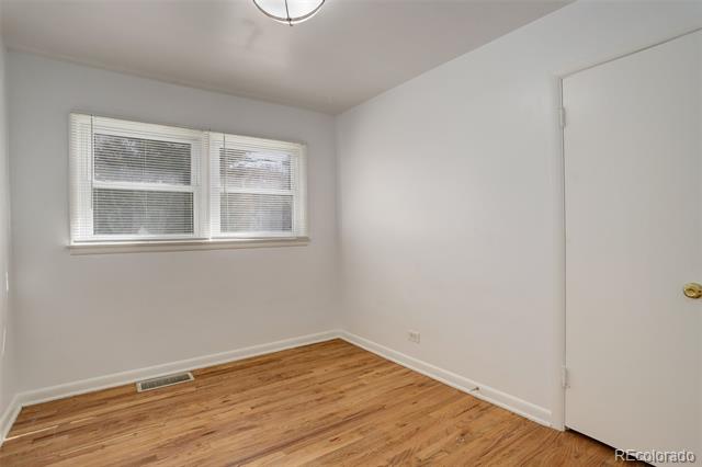 Empty room with hardwood floors, a double window with blinds, and a closed door.