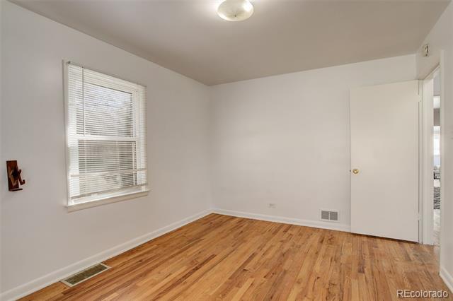 Empty bedroom with hardwood floors, window blinds, and an open door.