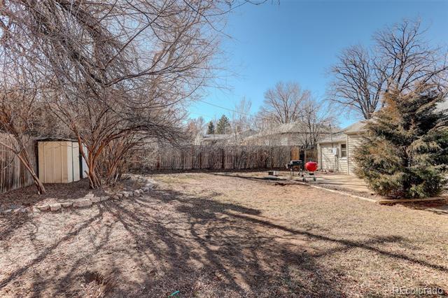 Backyard with dormant grass, leafless trees, two sheds, and a small paved patio.