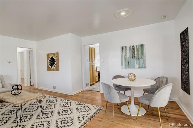 Dining area with a round white table, upholstered chairs, hardwood floors, and patterned rug.