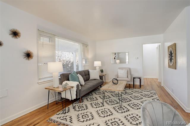 Living room with a gray sofa, patterned rug, and large windows with blinds.
