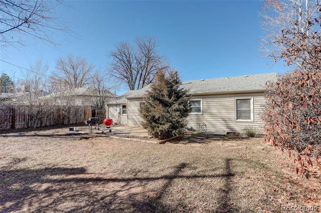 Single-story beige house viewed from a dry backyard, with a large evergreen shrub and leafless trees.