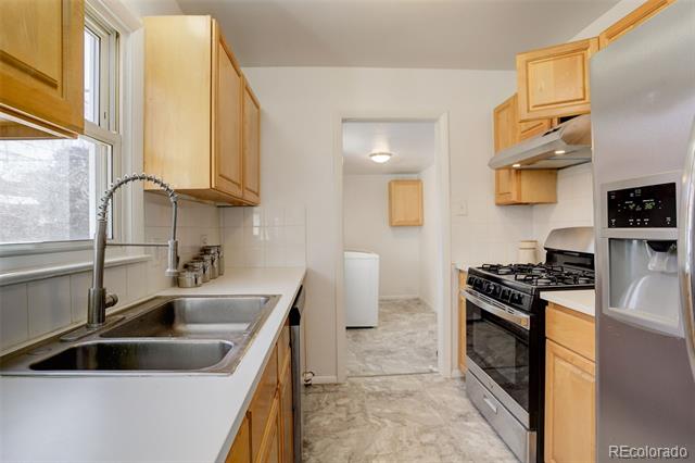 Kitchen with light wood cabinets, double-basin sink, gas range, and doorway to a utility area.