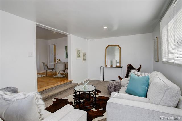 Living room with white sofas, a turquoise pillow, a glass coffee table, and a raised dining area.