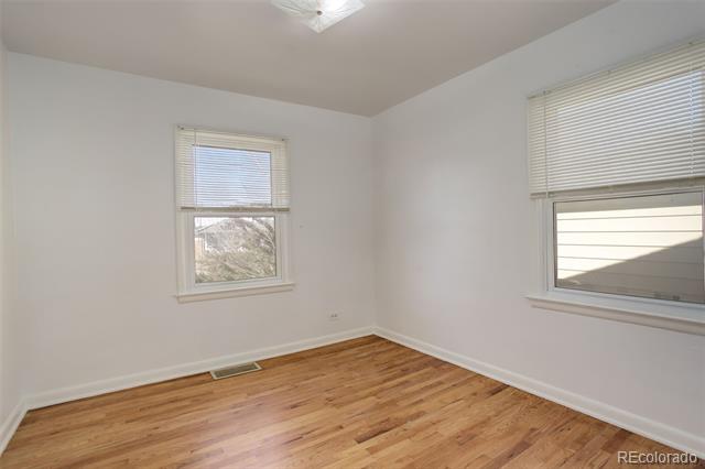 Empty room with hardwood floors and two windows with blinds; a mountain is visible outside.