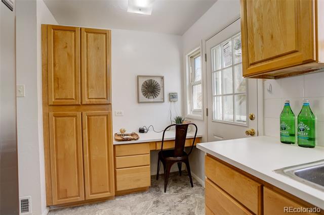 Kitchen with honey-colored cabinets, a built-in desk and chair, and a glass-paneled door.