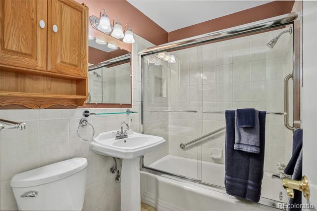 Bathroom with a glass-enclosed tub and shower, pedestal sink, and wooden wall cabinet.