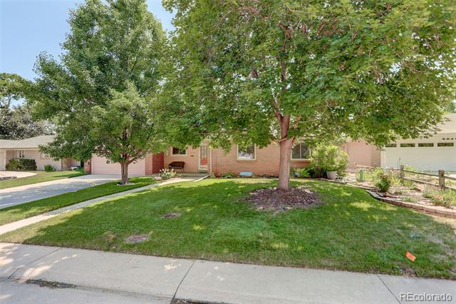 Brick house partly screened by two mature trees, with a front lawn, driveway, and attached garage.